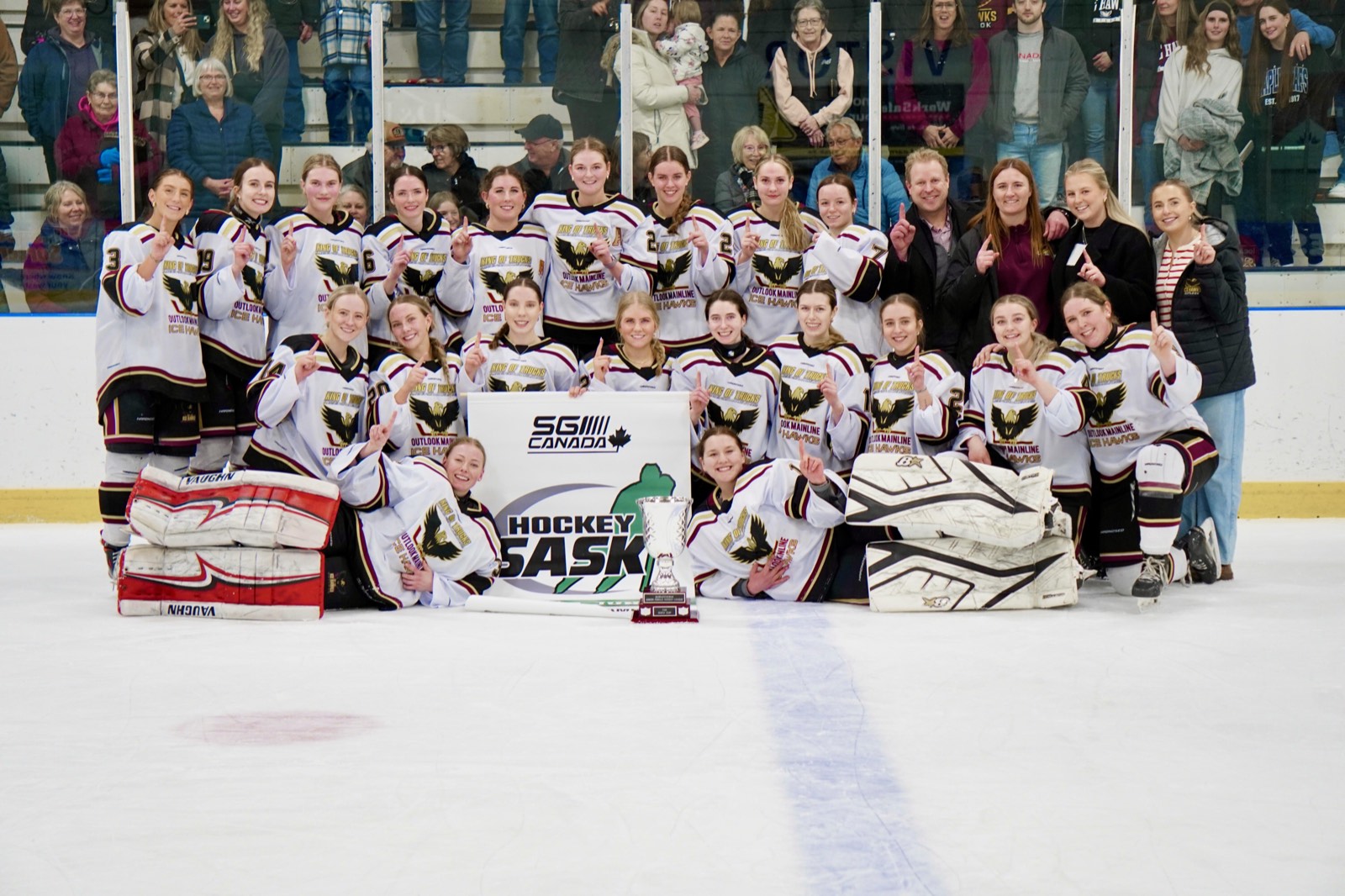 The Outlook Ice Hawks celebrating their 2025/26 SJFHL championship on the ice with the Hockey Sask banner and trophy